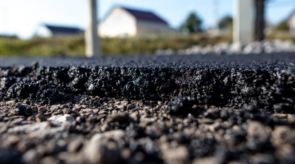 An image of freshly poured asphalt with a home in the background.